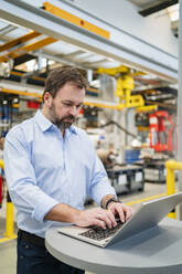 Manager typing on laptop at table in factory - DIGF20028