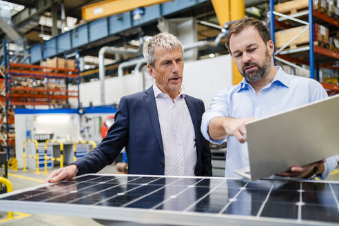 Manager holding laptop by businessman holding solar panel at factory - DIGF20030