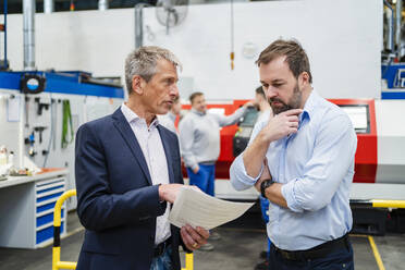 Businessman discussing with manager over document at factory - DIGF20044