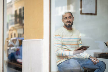 Man with tablet PC sitting at cafe seen through glass window - JOSEF18594