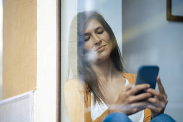 Frau, die ein Smartphone benutzt und sich an ein Glasfenster eines Cafés lehnt - JOSEF18644