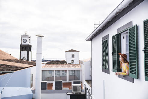 Woman with hat leaning on window of hotel - PCLF00426