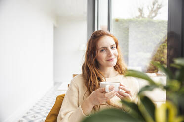 Smiling woman holding coffee cup by window - PCLF00434