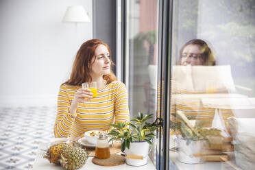 Frau hält ein Saftglas in der Hand und schaut aus dem Fenster - PCLF00441