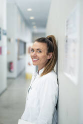 Smiling doctor leaning on wall at hospital - MOEF04540