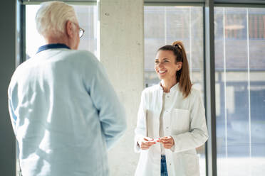 Lächelnder Arzt im Gespräch mit einem älteren Patienten im Krankenhaus - MOEF04546