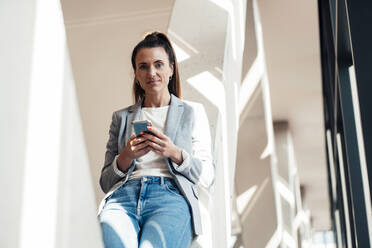 Young businesswoman holding mobile phone at office - MOEF04569