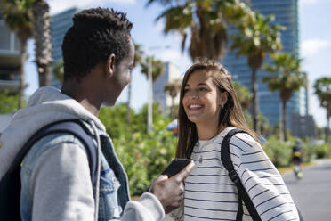 Smiling woman talking to friend holding smart phone at park - IKF00230