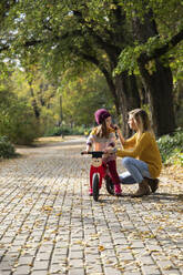 Mother assisting daughter sitting on bicycle at park - IKF00235