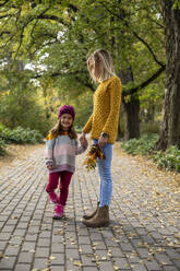 Smiling daughter holding mother's hand on footpath - IKF00238