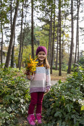 Smiling girl holding bunch of leaves - IKF00239