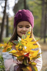 Cute girl wearing knit hat looking at leaves - IKF00241
