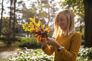 Young woman examining leaves at park - IKF00243