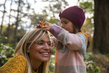 Daughter putting leaf in mother's hair - IKF00244