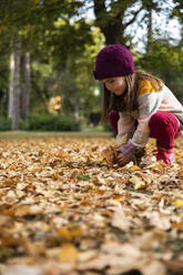 Girl picking up dry autumn leaves at park - IKF00248