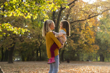 Mother carrying daughter in arms at autumn park - IKF00249