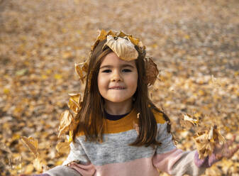 Lächelndes Mädchen, bedeckt mit trockenen Blättern im Herbstpark - IKF00250