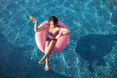 Frau hält Getränk schwimmend im Schwimmbad am sonnigen Tag - IKF00258