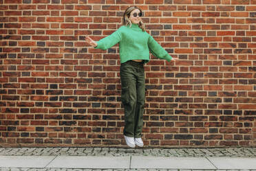 Teenager-Mädchen springt vor eine Ziegelmauer - VSNF00716