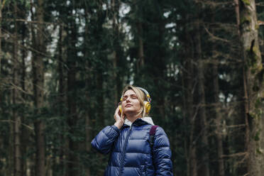 Young woman enjoying music through headphones in forest - VSNF00723