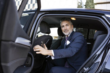 Businessman holding smart phone sitting in car - JJF00788