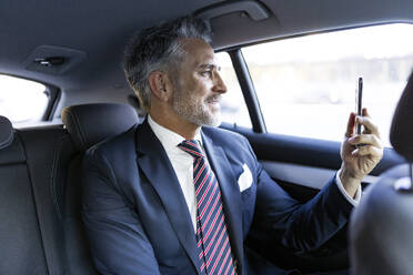 Smiling businessman doing video call through smart phone sitting in car - JJF00792