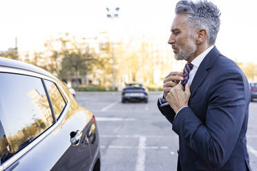 Businessman adjusting tie looking in car window - JJF00797