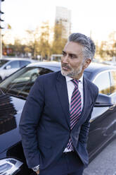 Contemplative businessman wearing suit leaning on car - JJF00800
