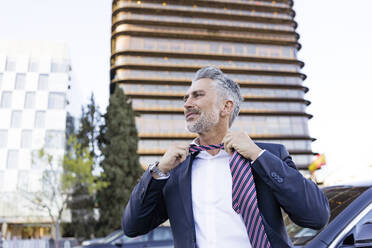 Mature businessman removing tie in front of building - JJF00803