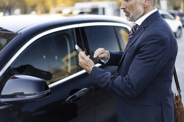 Businessman using smart phone standing near car - JJF00812