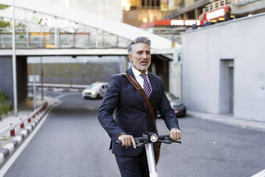 Mature businessman riding electric scooter on road - JJF00820
