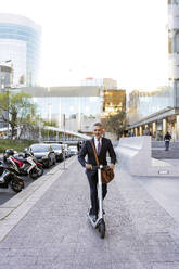 Mature businessman riding electric scooter on sidewalk - JJF00822