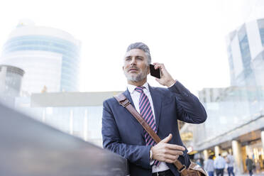 Businessman talking on smart phone leaning on wall - JJF00831