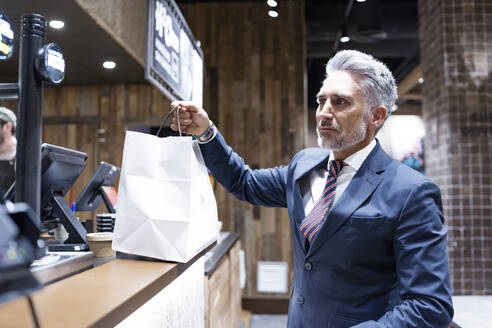 Businessman holding shopping bag standing at cafe counter - JJF00846