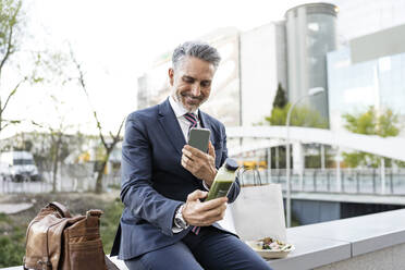 Lächelnder Geschäftsmann, der mit seinem Smartphone ein Bild von einer Smoothie-Flasche macht - JJF00855