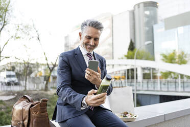 Smiling businessman taking picture of smoothie bottle through smart phone - JJF00855