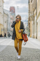 Stilvolle reife Frau, die mit ihrem Handy telefoniert und auf der Straße spazieren geht - VSNF00726