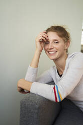 Smiling young woman leaning on sofa - PNEF02672