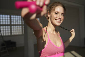 Smiling woman holding skipping rope - PNEF02674