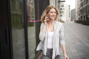 Lächelnde blonde Frau, die mit einem Mobiltelefon spricht - PNEF02687