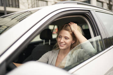Lächelnde Frau mit Hand im Haar beim Autofahren - PNEF02703