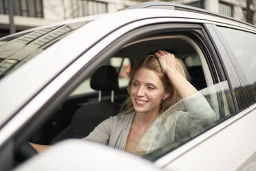 Smiling woman with hand in hair driving car - PNEF02703