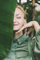 Smiling woman with banana leaf over face - NDEF00577