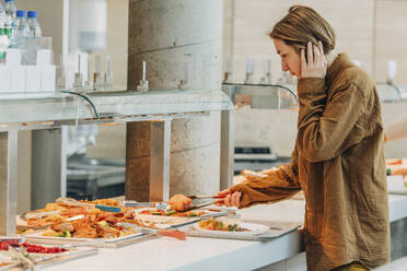 Woman taking food in plate standing by buffet - VSNF00730