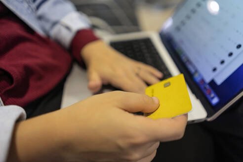 Junge Frau beim Online-Shopping mit Kreditkarte und Laptop in der Flughafen-Lobby - JJF00874