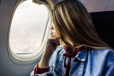Frau mit Hand am Kinn schaut aus dem Flugzeugfenster - JJF00875