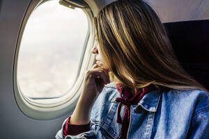 Frau mit Hand am Kinn schaut aus dem Flugzeugfenster - JJF00875