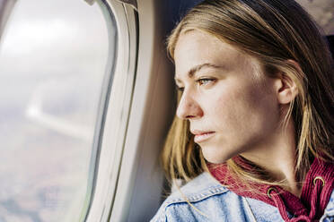 Young woman looking out of airplane window - JJF00876