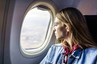 Frau schaut im Flugzeug sitzend aus dem Fenster - JJF00877