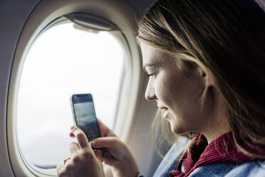 Woman photographing through smart phone in airplane - JJF00878